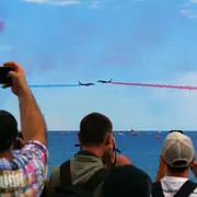 Spectateurs photographiant deux avions avec des panaches bleu et rouge